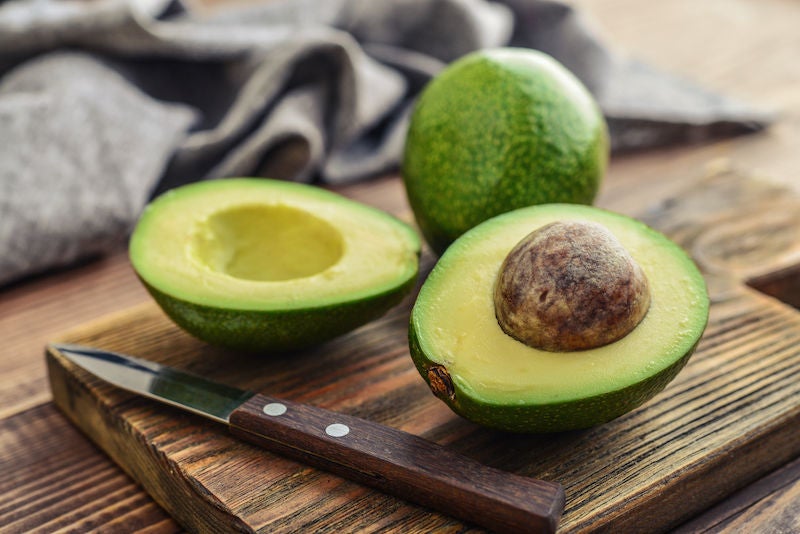 Fresh avocado on cutting board over wooden background