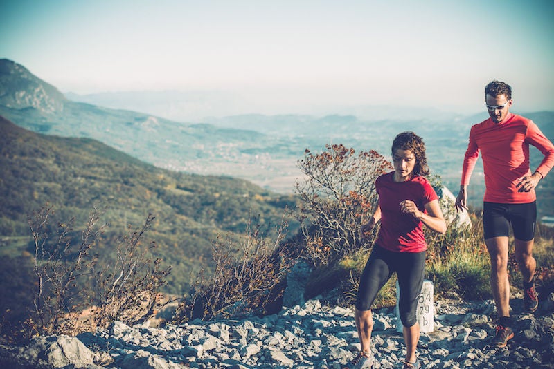 Young couple running uphill on the mountain in Julian Alps, Italia-Slovenia border, Europe.  Smokebush growing among gray limestone. Very windy, woman's hair is blowing in the wind. SoÄ a valley. Nikon D800, full frame, XXXL.